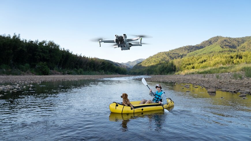 Dron DJI Mini 3 Fly More Combo CP.MA.00000613.01 latający nad wodą oraz mężczyzna z psem płynący na pontonie