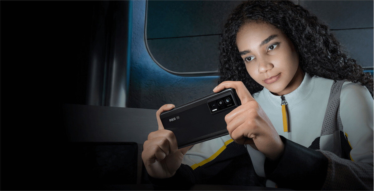 Smartfon Xiaomi POCO F5 Pro 12 + 256GB czarny kobieta siedząca w ciemnym pomieszczeniu z włączonym telefonem w rekach