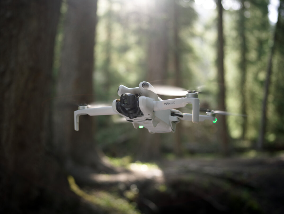 Dron DJI Mini 4 Pro Fly More Combo (DJI RC 2) grafika przedstawiająca dron po skosie unoszący się nad ziemią w lesie