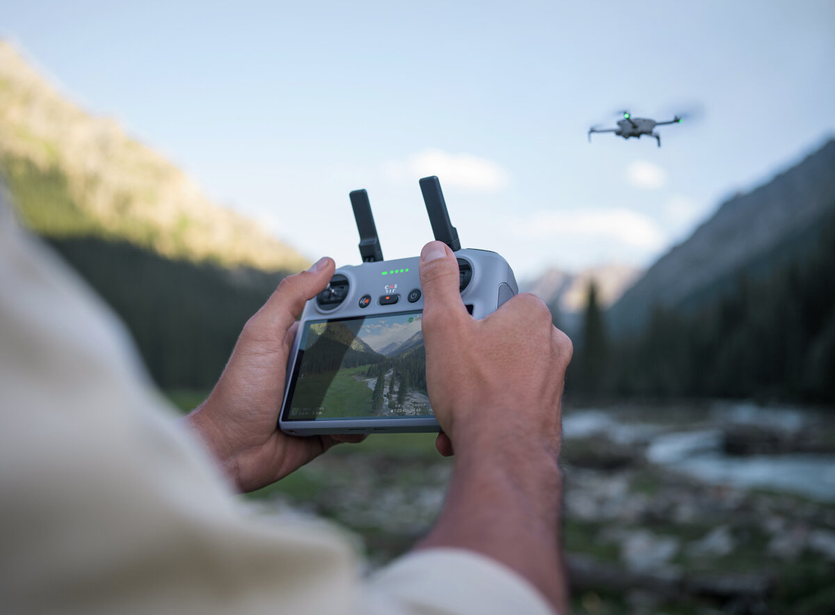 Dron DJI Mini 4 Pro Fly More Combo (DJI RC 2) grafika przedstawiająca mężczyznę sterującego dronem przez kontroler nad potokiem